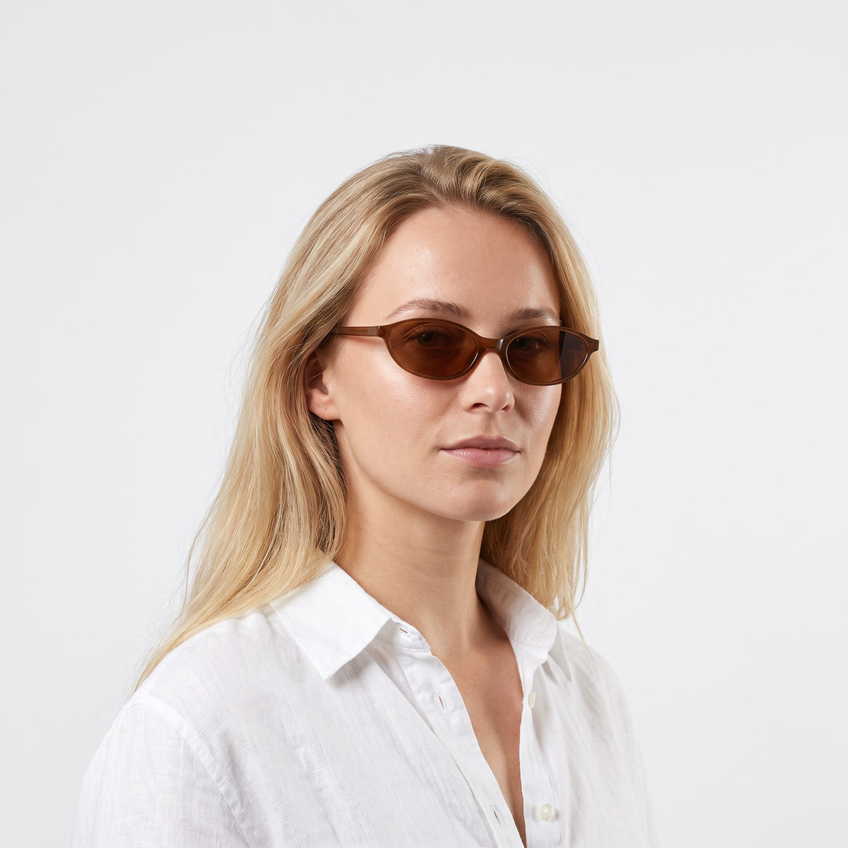 Woman in a white linen shirt wearing Malibu slim oval translucent brown sunglasses with brown lenses · Velezeco #opt1_3