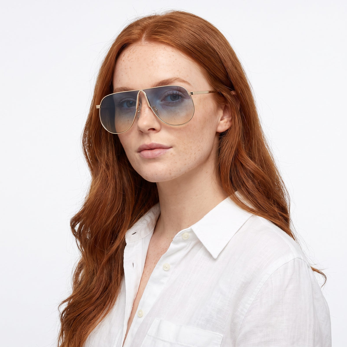 Woman in a white linen shirt wearing Mirage oversized gold shield aviator sunglasses with blue to yellow gradient lenses, Blue Yellow · Velezeco #opt1_3