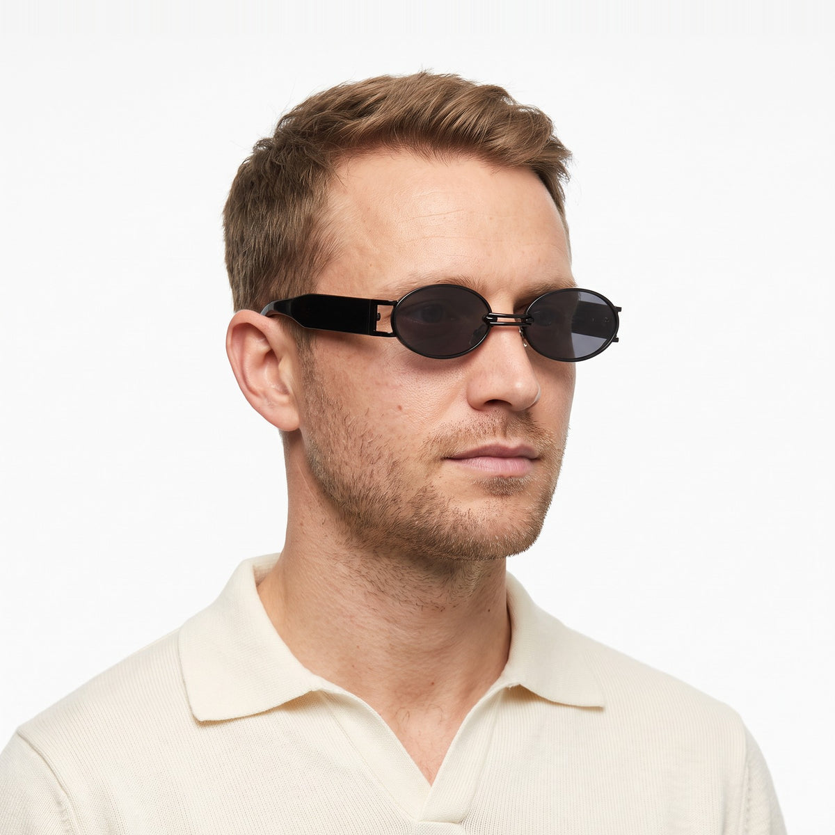 Man in a cream knit polo wearing Monte Carlo black oval sunglasses with dark grey lenses · Velezeco #opt1_3