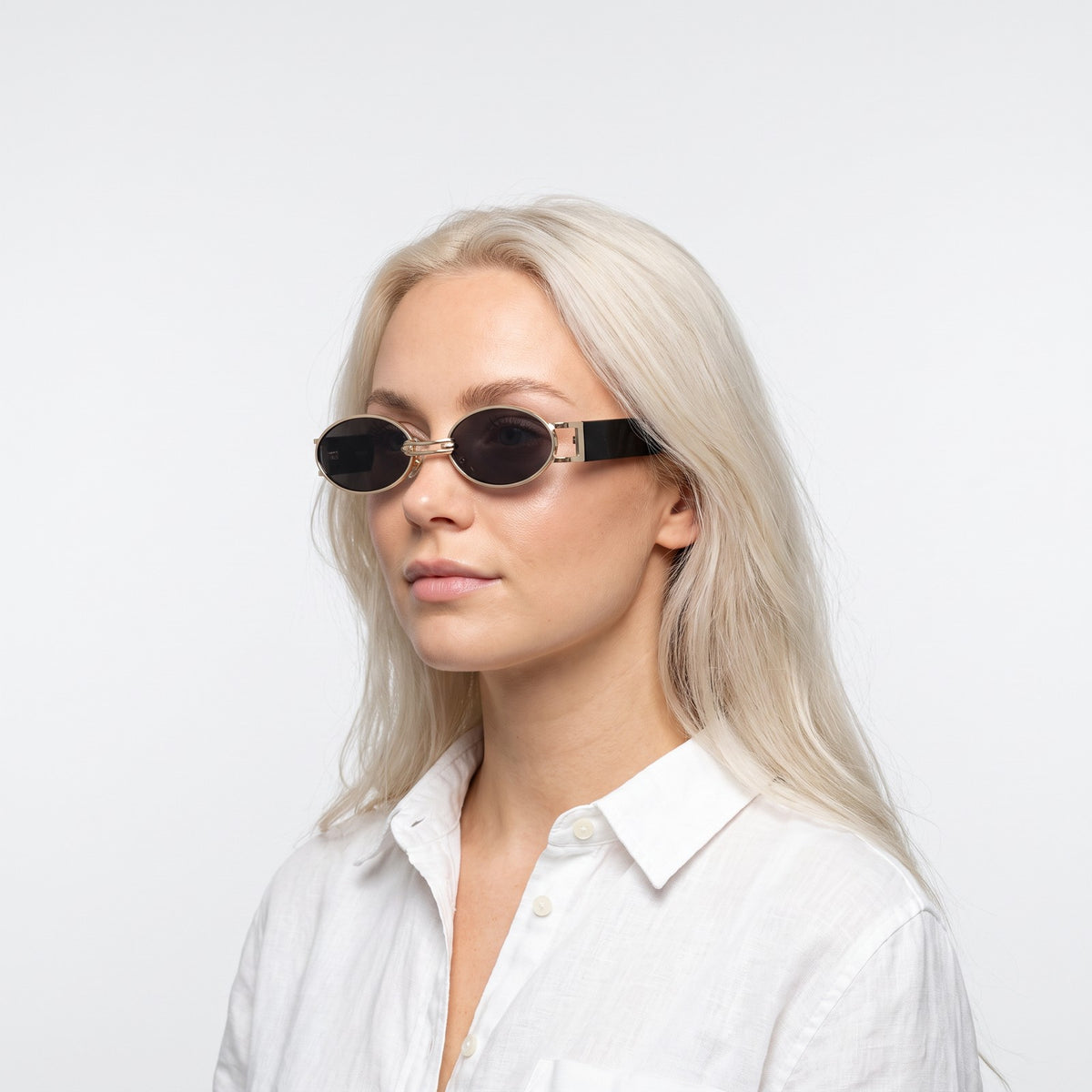 Woman in a white linen shirt wearing Monte Carlo gold oval sunglasses with dark grey lenses and black temples · Velezeco #opt1_2