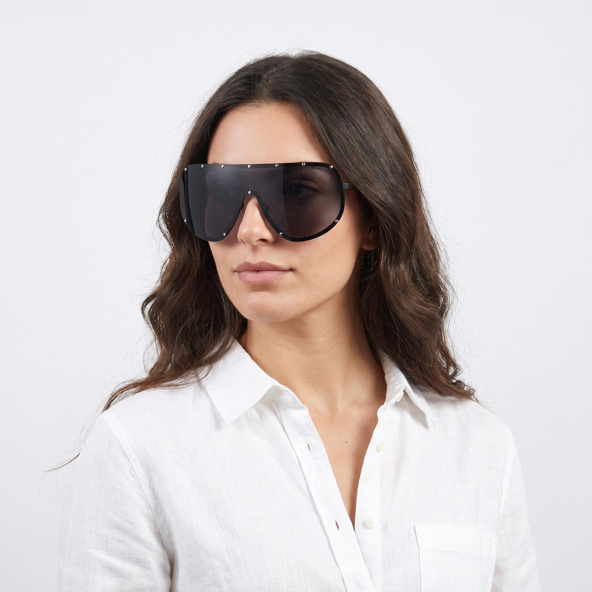 Woman in a white linen shirt wearing Mykonos shield sunglasses with black studded rim and solid grey lens — Velezeco #opt1_1