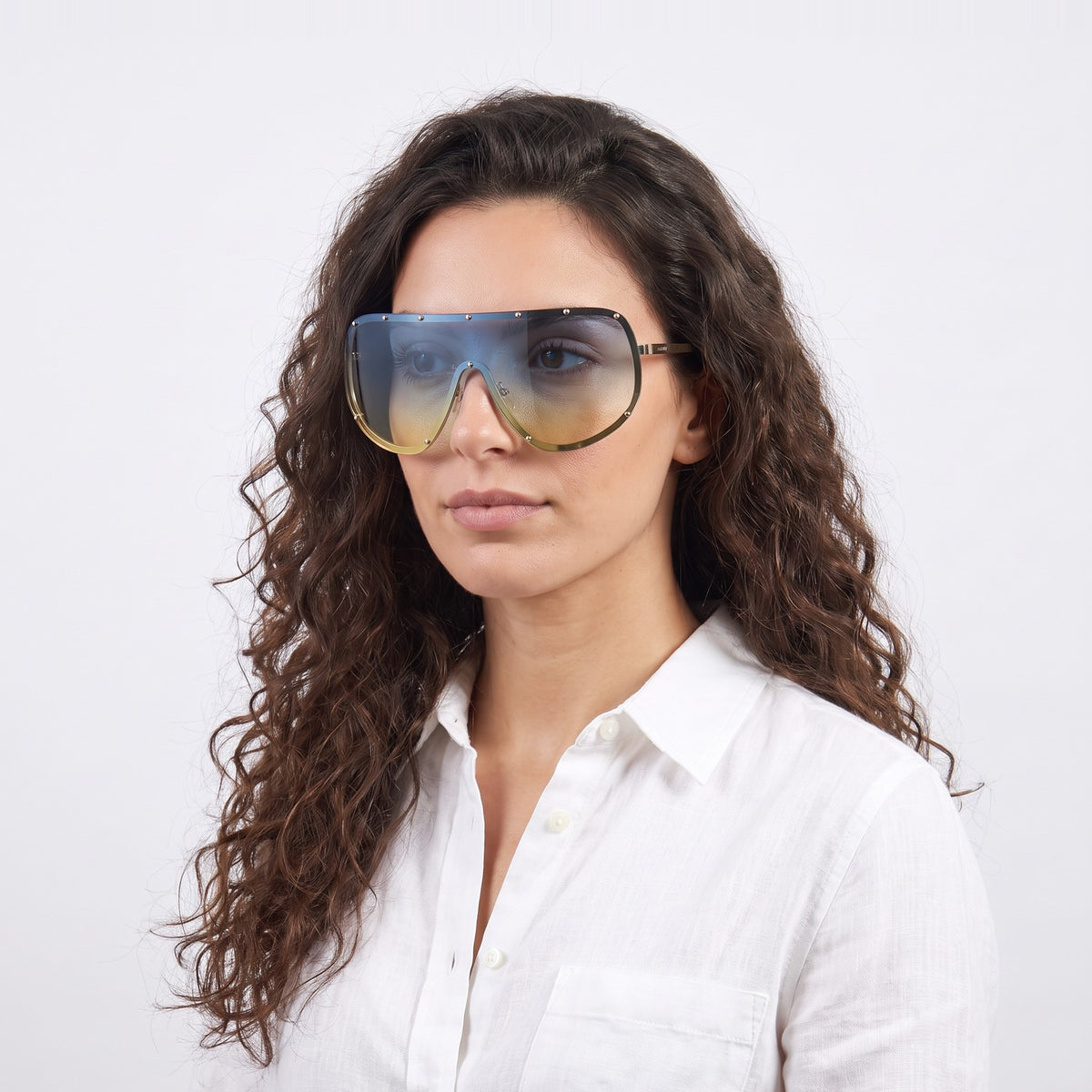 Woman in a white linen shirt wearing Mykonos shield sunglasses with gold studded rim and blue-to-yellow gradient lens — Velezeco #opt1_7