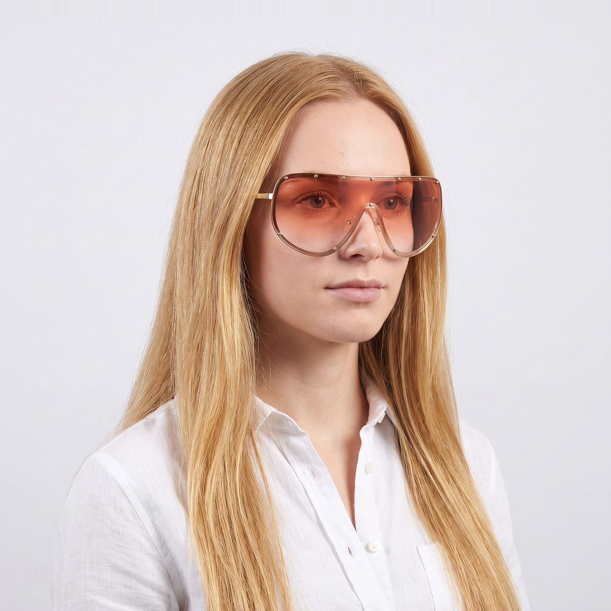 Woman in a white linen shirt wearing Mykonos shield sunglasses with gold studded rim and pink gradient lens — Velezeco #opt1_5