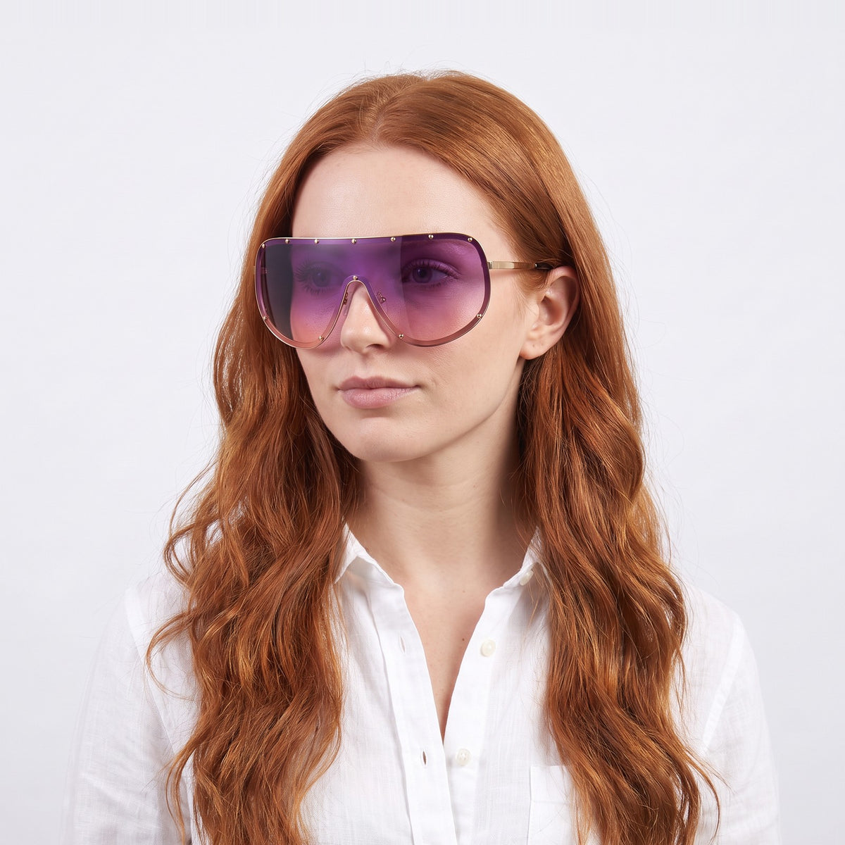 Woman in a white linen shirt wearing Mykonos shield sunglasses with gold studded rim and purple-to-pink gradient lens — Velezeco #opt1_6
