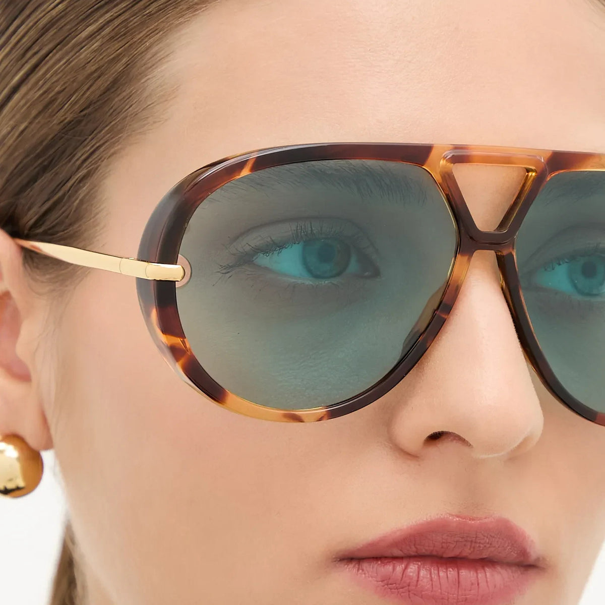Close-up of The Nimbus oversized tortoiseshell aviator sunglasses with blue lenses and gold temples on a model, studio portrait — Velezeco #opt1_5