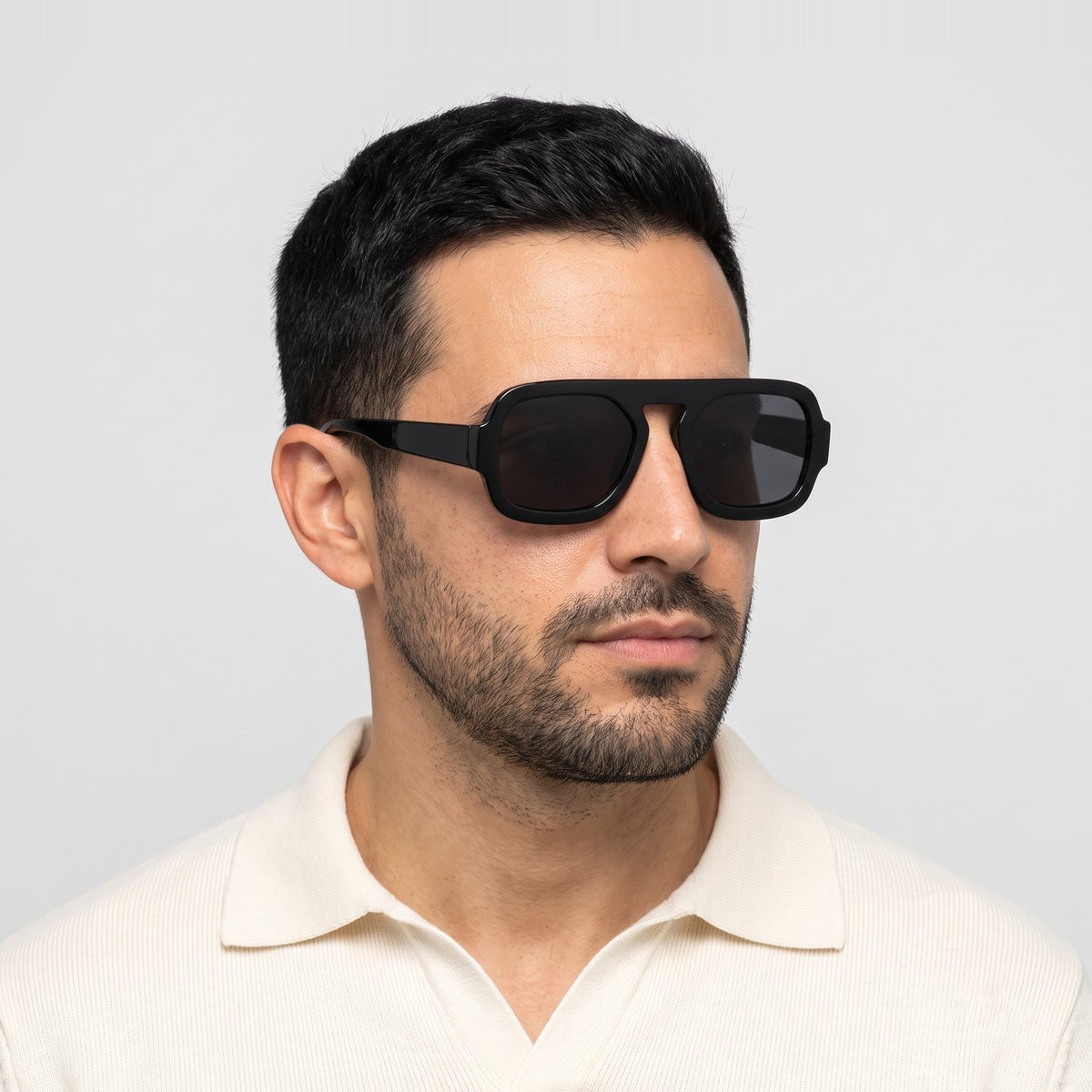 Man in a cream knit polo wearing Vortex black square pilot sunglasses with dark grey lenses · Velezeco #opt1_3