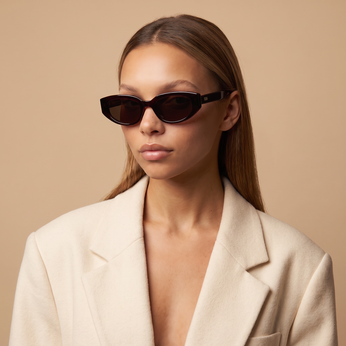 Woman wearing Astra polarized sunglasses in black cherry red with dark brown lenses and a cream blazer — Velezeco