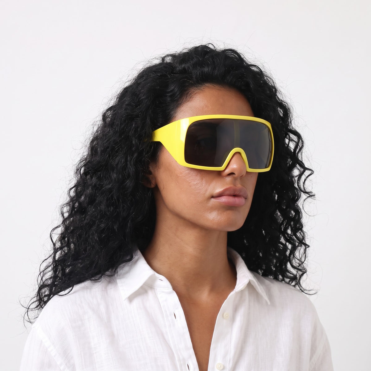 Woman in a white linen shirt wearing Berlin wrap shield sunglasses with glossy yellow frame and grey lens — Velezeco #opt1_6
