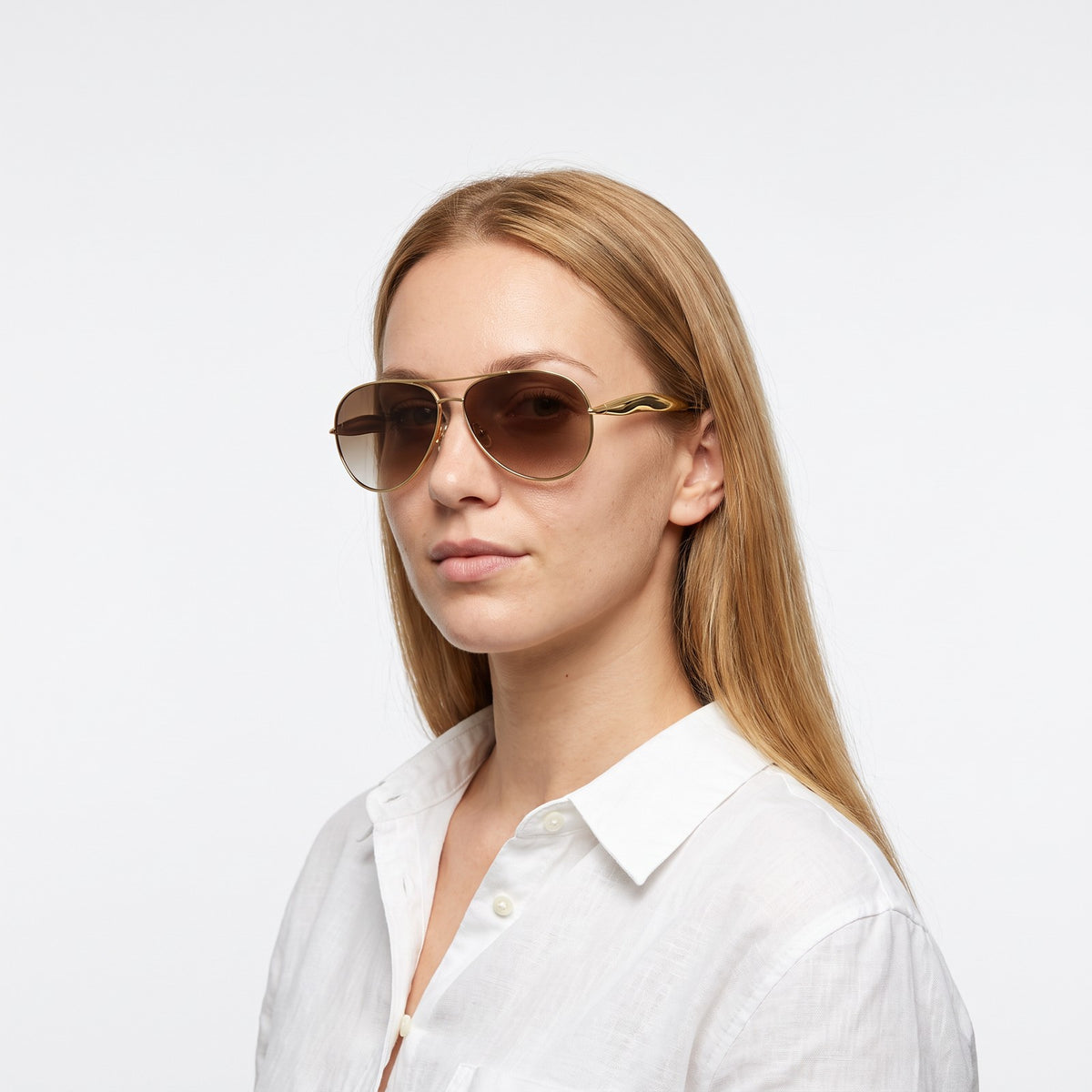 Woman in a white linen shirt wearing Duna gold aviator sunglasses with brown gradient lenses · Velezeco #opt1_6
