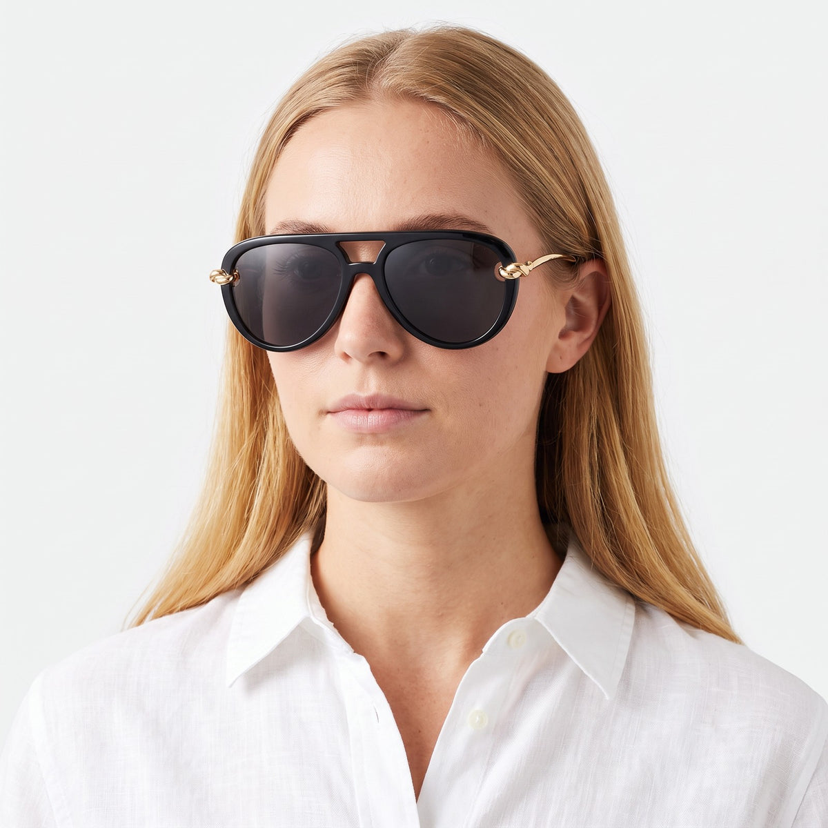Woman in a white linen shirt wearing Lunna black aviator sunglasses with dark grey lenses and gold knot temples · Velezeco #opt1_2