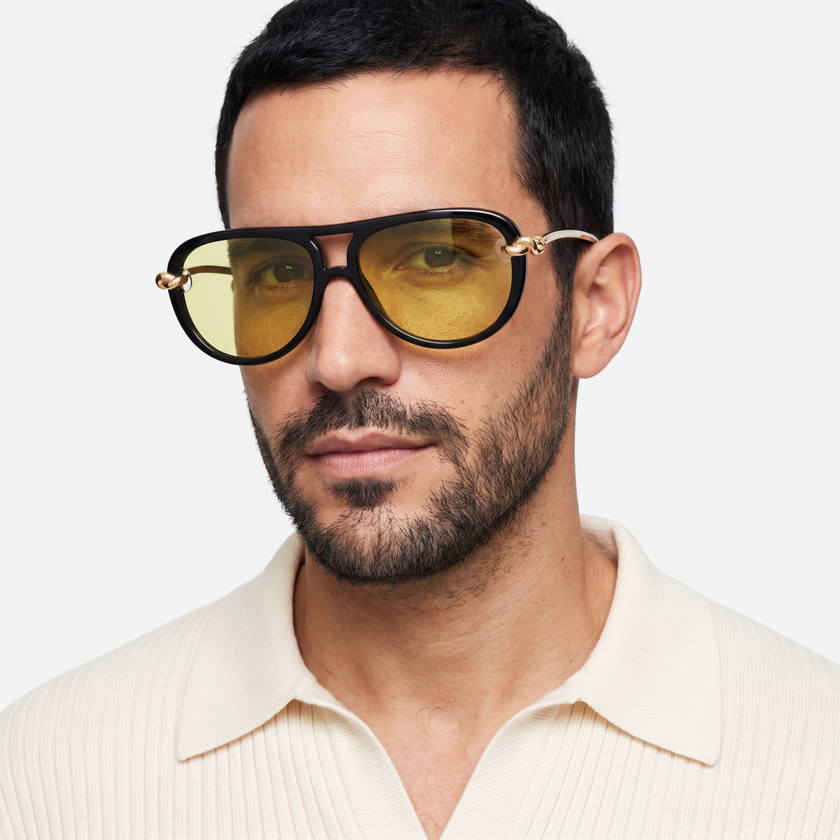 Man in a cream knit polo wearing Lunna black aviator sunglasses with yellow lenses and gold knot temples · Velezeco #opt1_1