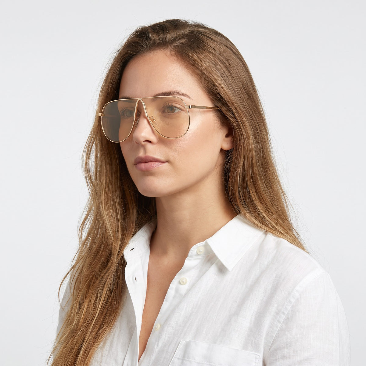 Woman in a white linen shirt wearing Mirage oversized gold shield aviator sunglasses with champagne lenses, Champagne · Velezeco #opt1_1