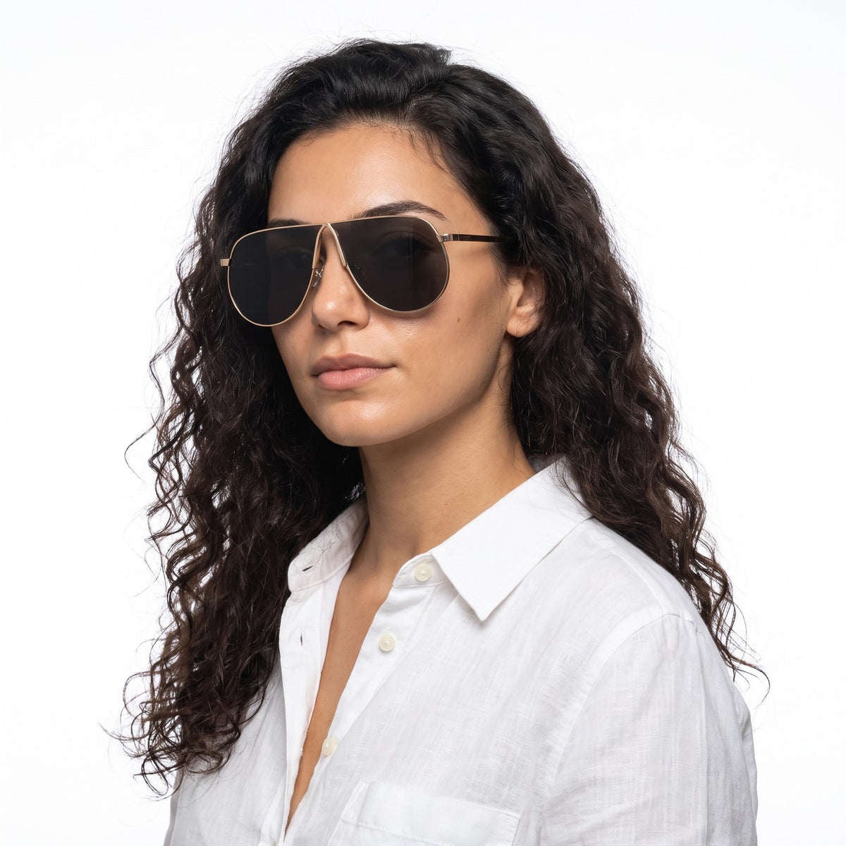 Woman in a white linen shirt wearing Mirage oversized gold shield aviator sunglasses with dark grey lenses, Gold · Velezeco #opt1_4