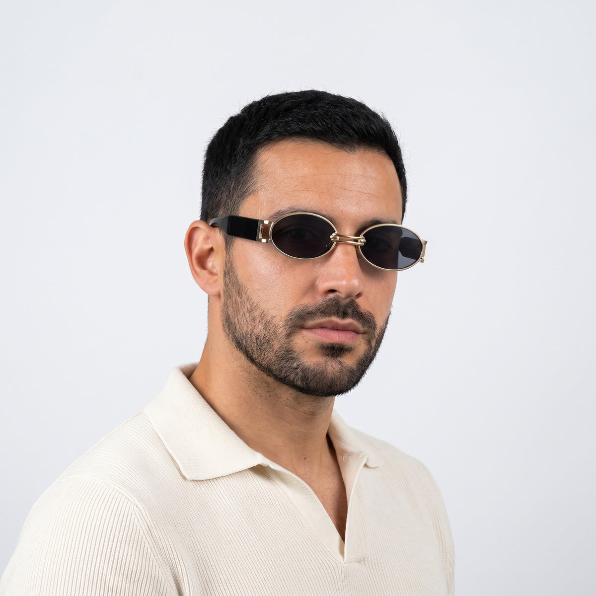 Man in a cream knit polo wearing Monte Carlo gold oval sunglasses with dark grey lenses and black temples · Velezeco #opt1_2