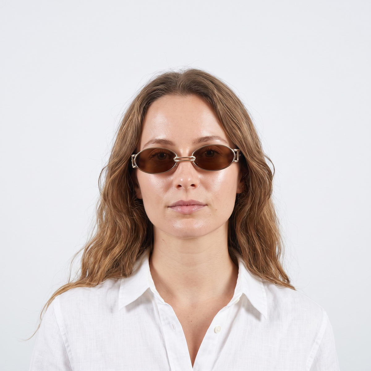 Woman in a white linen shirt wearing Monte Carlo gold oval sunglasses with brown lenses and brown temples · Velezeco #opt1_1