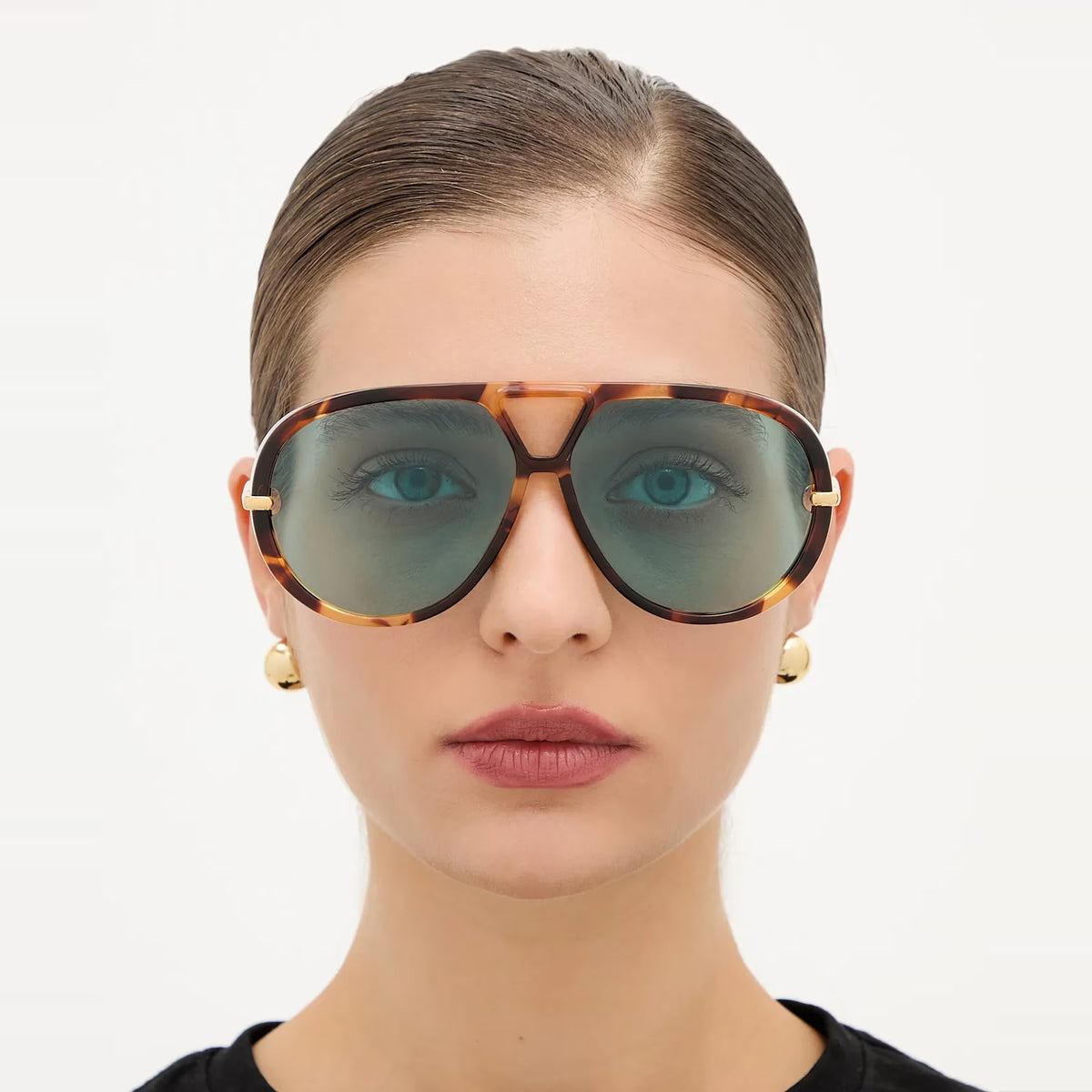 Woman wearing The Nimbus oversized tortoiseshell aviator sunglasses with blue lenses, triangle bridge and gold drop temples, studio portrait — Velezeco #opt1_5